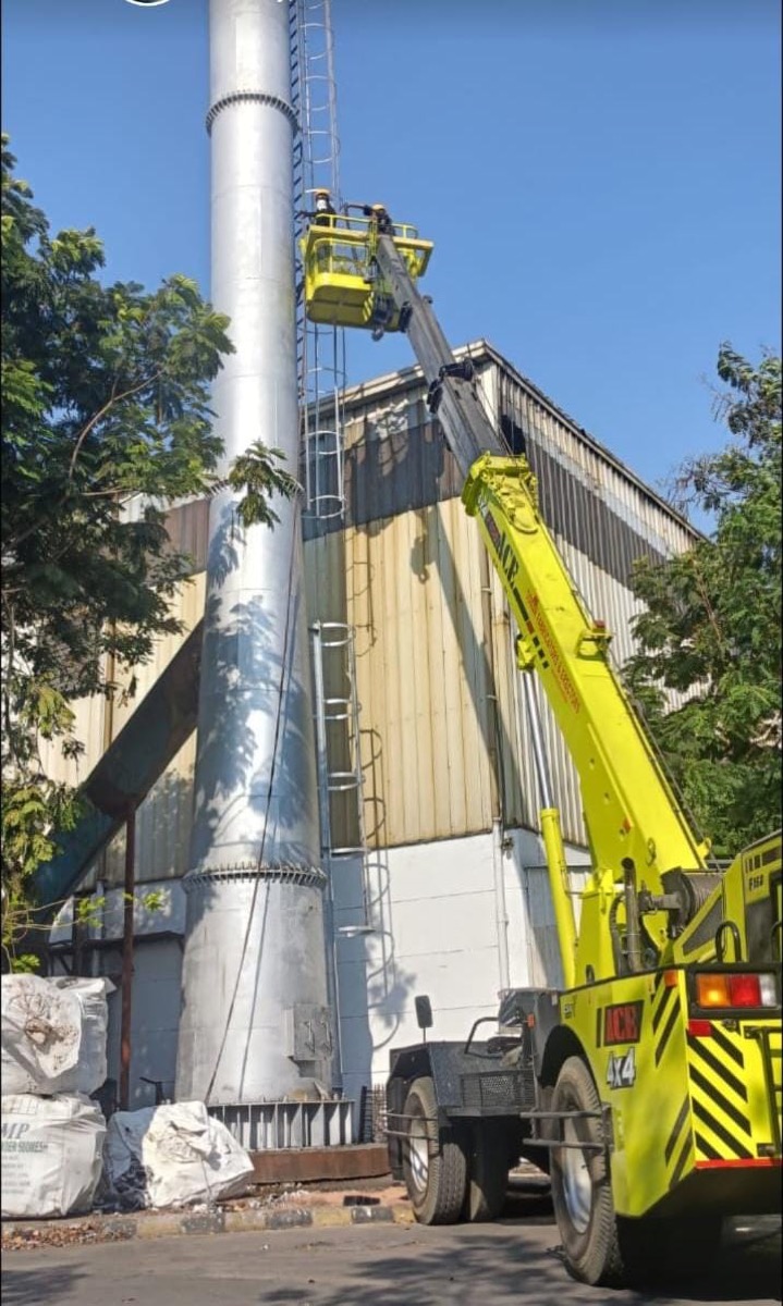 Industrial exhaust chimney being lifted into position by mobile crane with a cage platform for workers at height