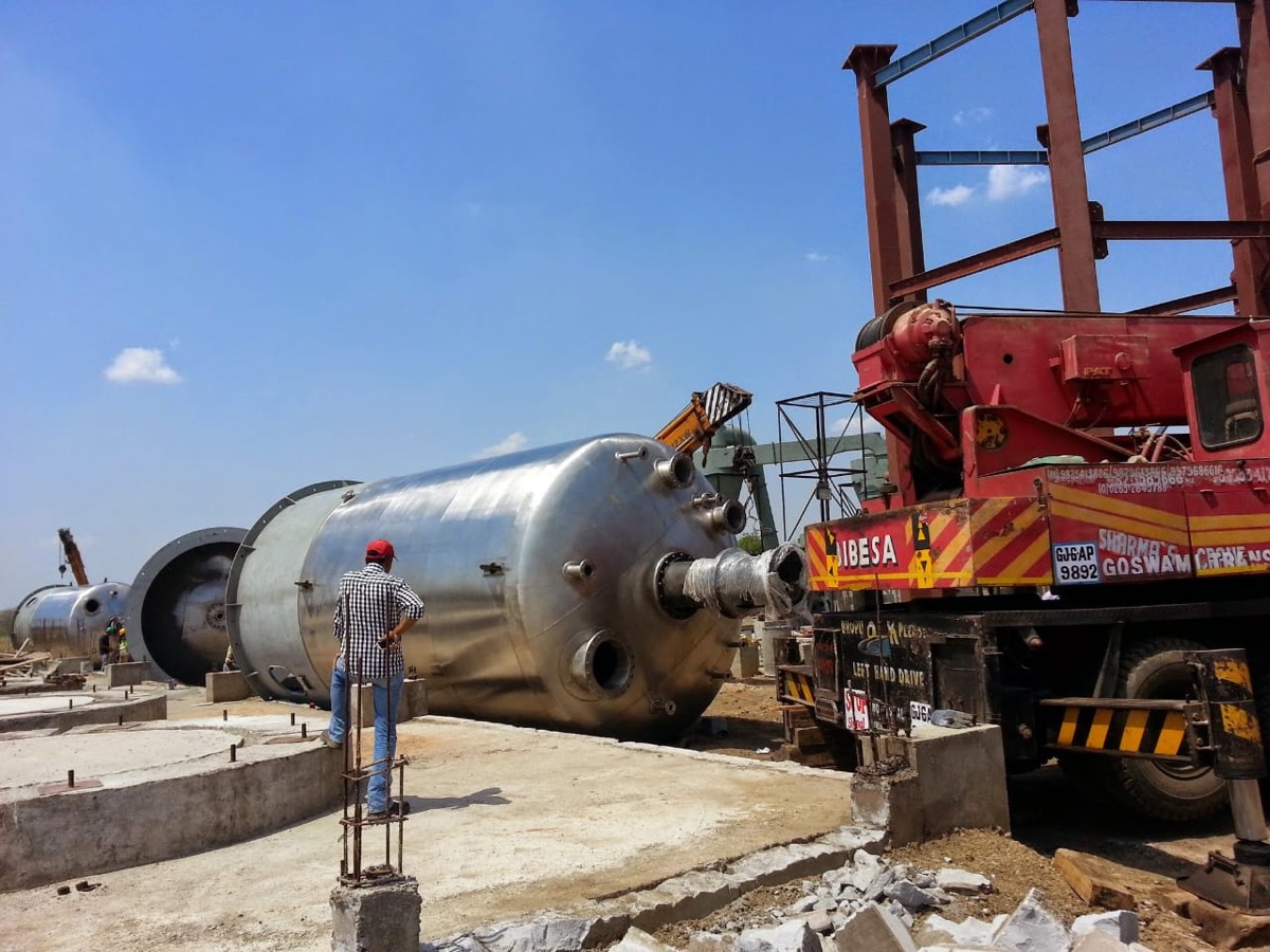 Large cylindrical storage vessel being lifted and positioned by mobile crane at site